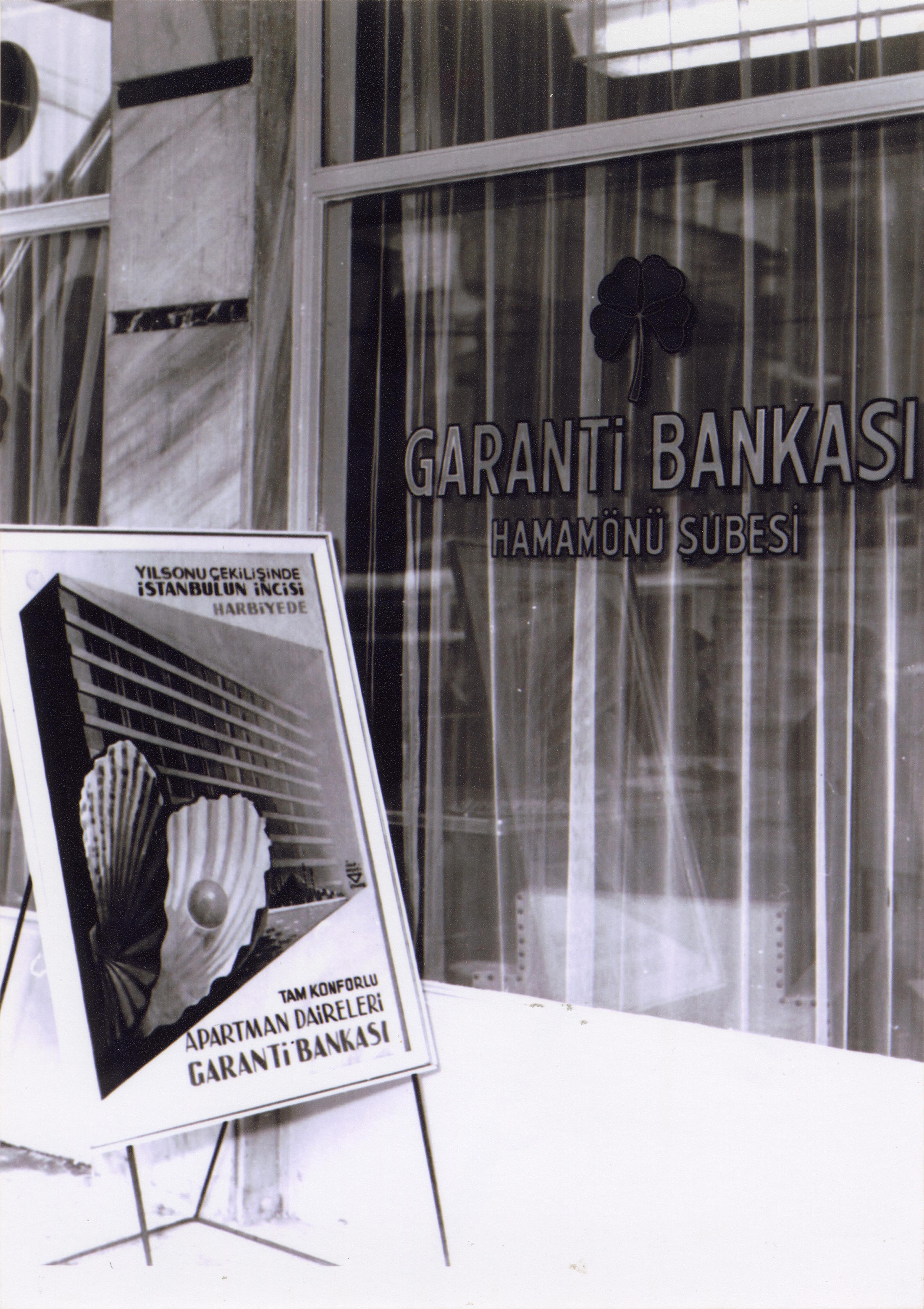 Garanti Bankası Hamamönü Şubesi (Ankara) ve önünde İhap Hulusi Görey’in tasarladığı apartman çekilişi afişi, 1950’ler Salt Araştırma, Garanti BBVA Arşivi