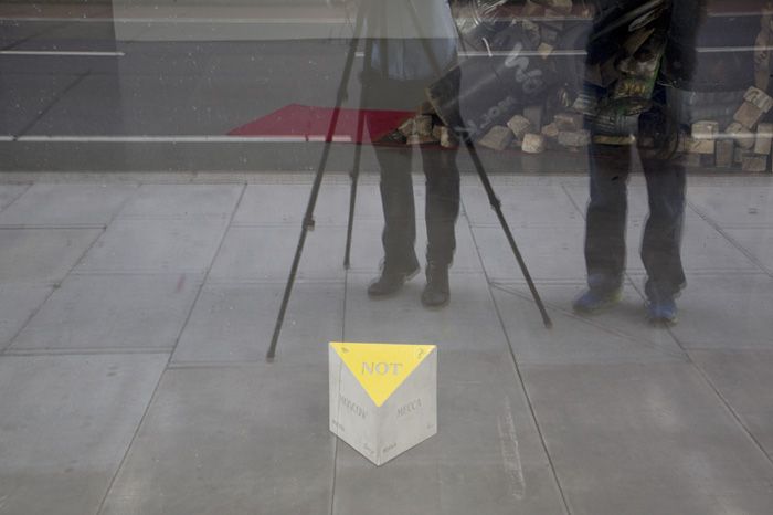 Triangulation (Not Moscow -Not Mecca) Slavs & Tatars’ın 2011 tarihli <i>Triangulation (Not Moscow -Not Mecca)</i> adlı işinin, 2012’de Royal College of Art’ta düzenlenen <i>The Europa Triangle</i> sergisinin galeri camından görüntüsü; fotoğrafçı ve küratörün yansıması ile. Fotoğraf: Bryan Dooley. Sanatçıların ve Kraupa-Tuskany’nin (Berlin) izniyle